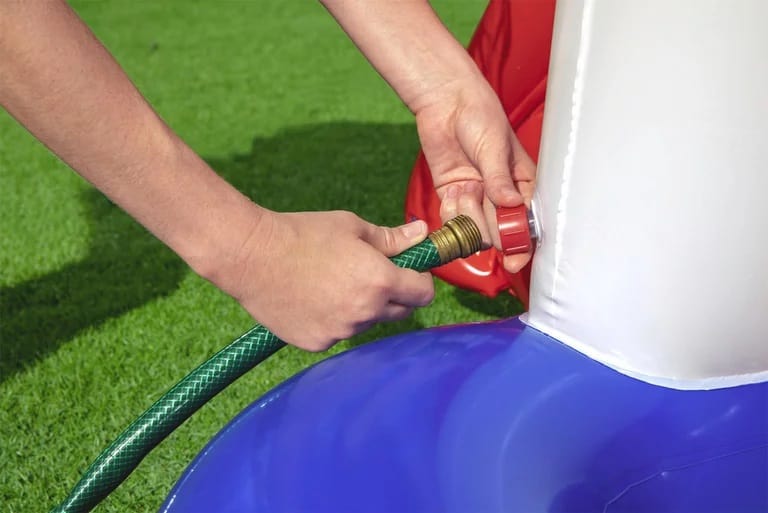 Alt-Text: Person verbindet Gartenschlauch mit Wasserpumpe auf Rasenfläche, Installation.