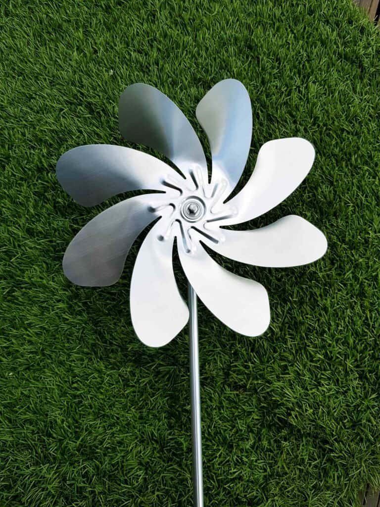Moderne Windmühlenflügel aus Metall auf grünem Rasen.